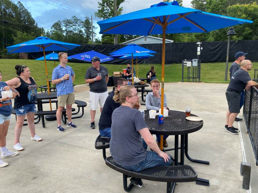 the logistiview team sitting around tables with blue umbrellas after watching a baseball game
